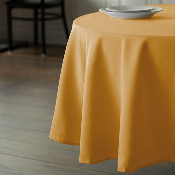 A yellow Intedge polyester tablecloth on a round table with a white plate.