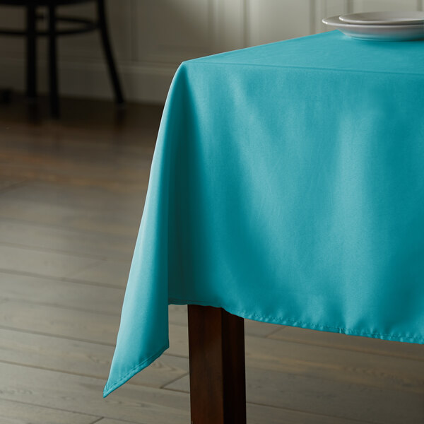 A table with a teal rectangular tablecloth on it.