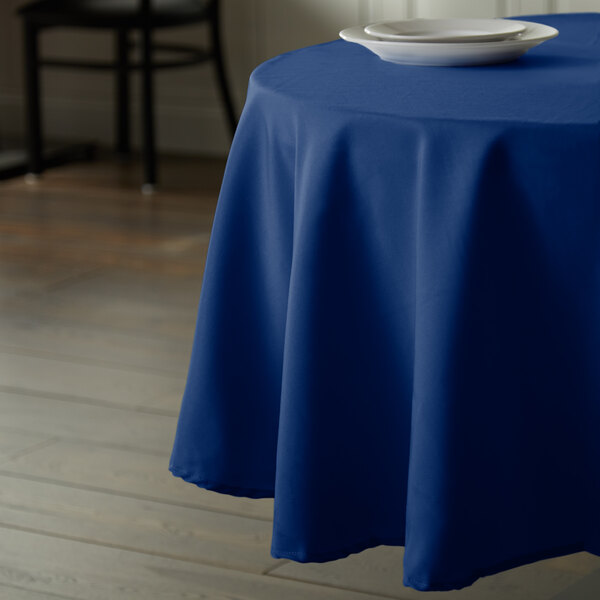 A blue Intedge tablecloth on a table with a white plate on it.