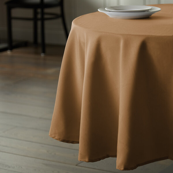 A table with a brown Intedge 72" round tablecloth on it with a plate.