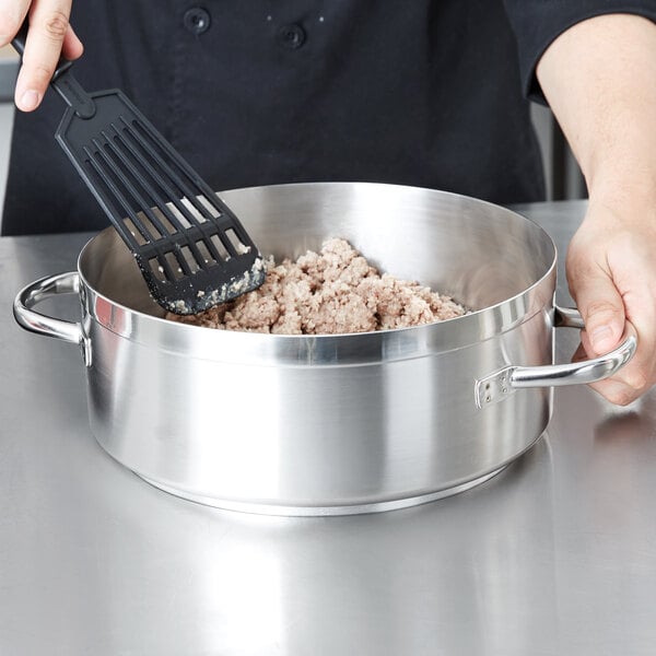 A person using a spatula to stir meat in a Vollrath Centurion brazier pan.