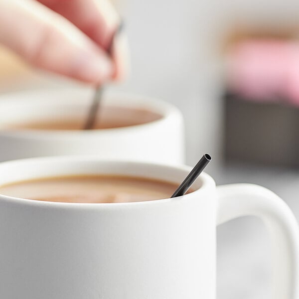 A person using a Choice black coffee stirrer in a mug of coffee.