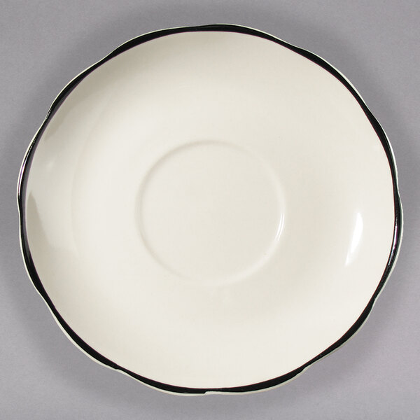 A white CAC saucer with scalloped edges and a black rim.