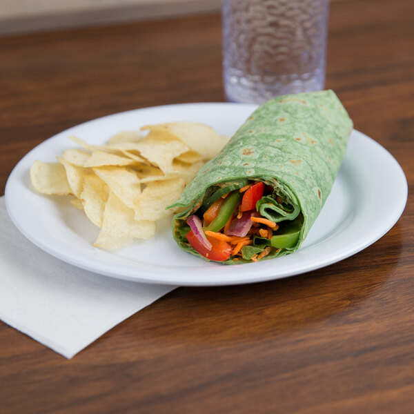A tortilla wrap with vegetables and chips on a white melamine plate.