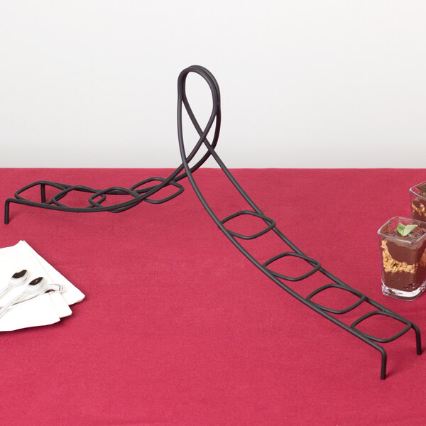 A black metal GET dessert shot display stand with chocolate desserts on a table.