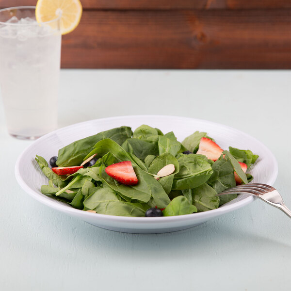 A white Minski melamine bowl filled with a salad of spinach, strawberries, and blueberries.