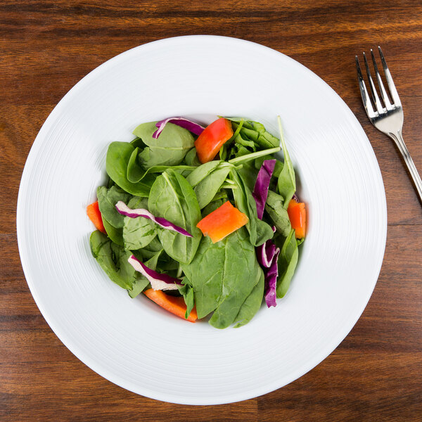 A Minski white melamine bowl filled with salad including spinach, carrots, and red cabbage with a fork.