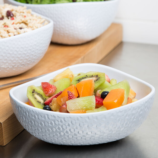 A white Coralline triangle bowl filled with fruit salad on a cutting board.