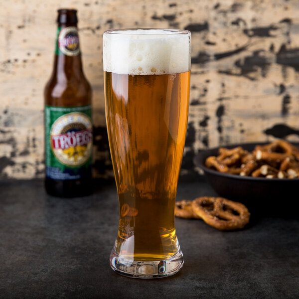 A GET Tritan plastic pilsner glass filled with beer on a table next to a bowl of pretzels.