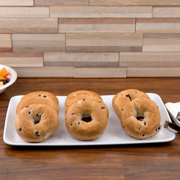 A white melamine display tray with bagels and a bowl of fruit on a table.