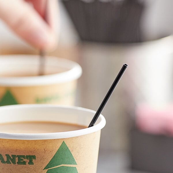 A person holding a cup of coffee with a black Choice coffee stirrer.