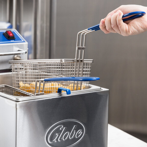 A hand using a Globe fryer basket with a blue handle to clean a deep fryer.