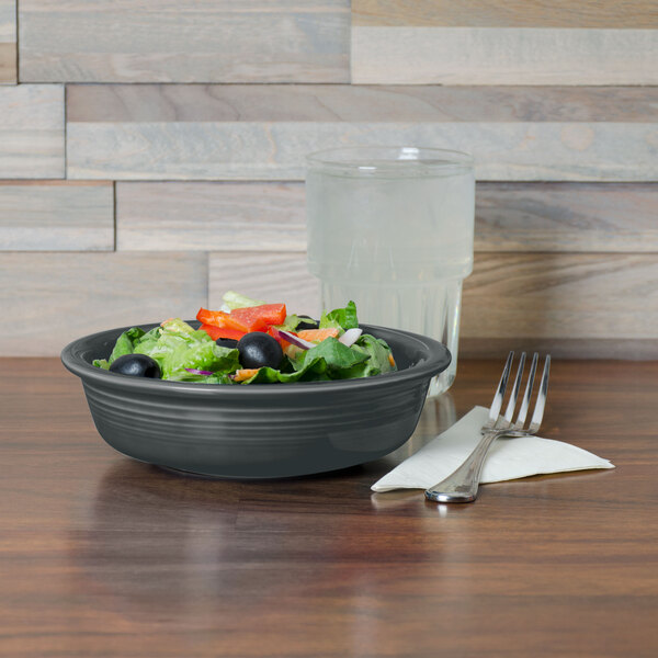 A Fiesta china bowl filled with salad on a table with a water glass.