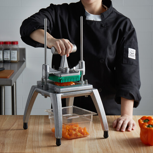 A woman in a chef's uniform using a Nemco Easy Chopper III to slice bell peppers on a table in a professional kitchen.