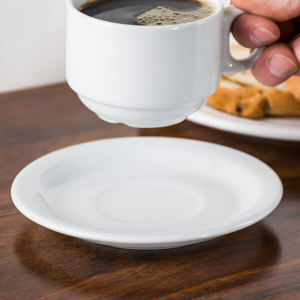 A hand holding a Tuxton white tea cup over a saucer.