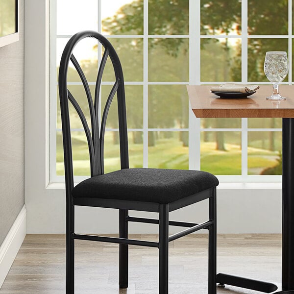 A black chair with a black fabric cushion next to a table.