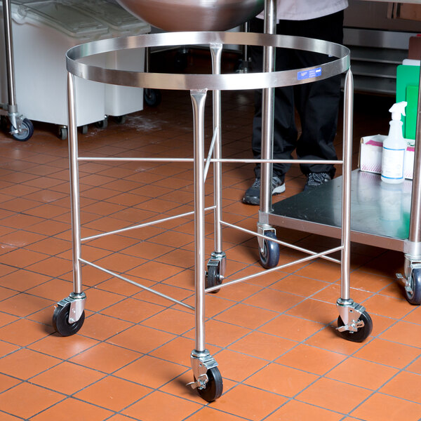 A man using a Vollrath stainless steel mobile mixing bowl stand.