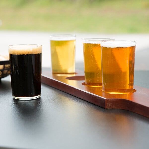 A row of Libbey straight sided tasting glasses of beer on a mahogany flight paddle.