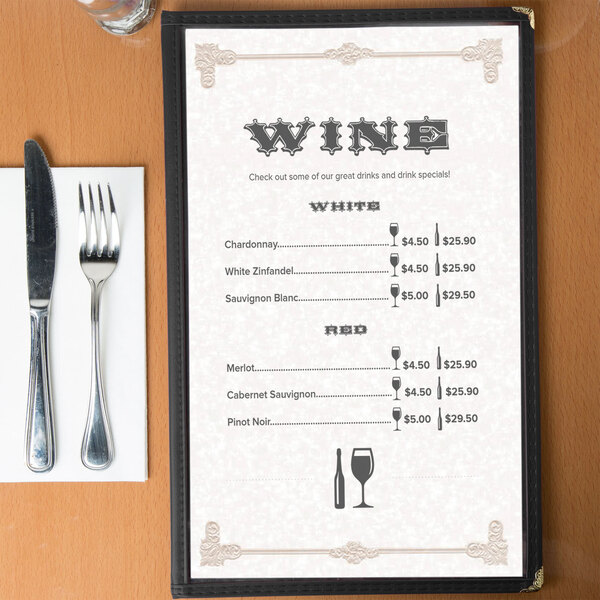 A tan menu with a scroll border on a table set with wine glasses, silverware, and menus.