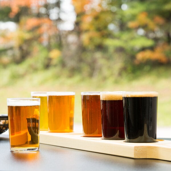 A row of Libbey Straight Sided Tasting Glasses on a natural flight paddle.