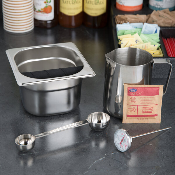 A stainless steel measuring cup and measuring spoons in a metal container with a handle.