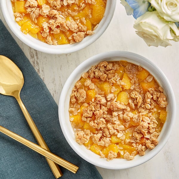 A bowl of fruit and crumble with a spoon next to a bowl of diced peaches.