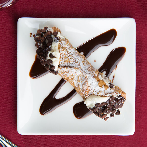 A cannoli on a 10 Strawberry Street white square bone china plate with chocolate sauce.