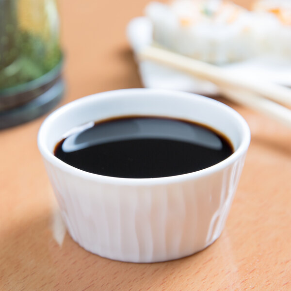 A white small porcelain ramekin filled with soy sauce on a table.