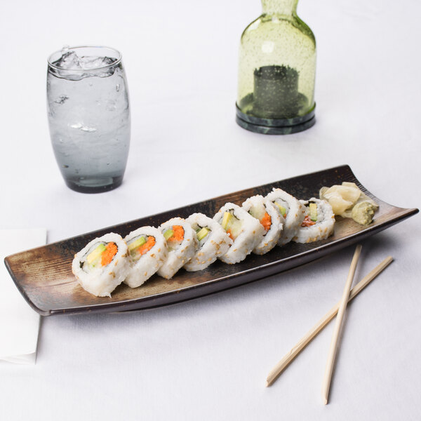 A rectangular stoneware platter with sushi rolls on a table.