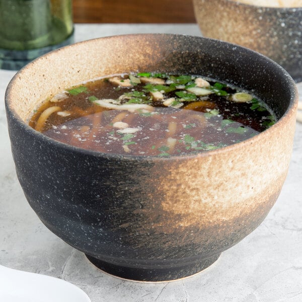 A 10 Strawberry Street Whittier Nagoya stoneware bowl filled with soup, noodles, and green onions.