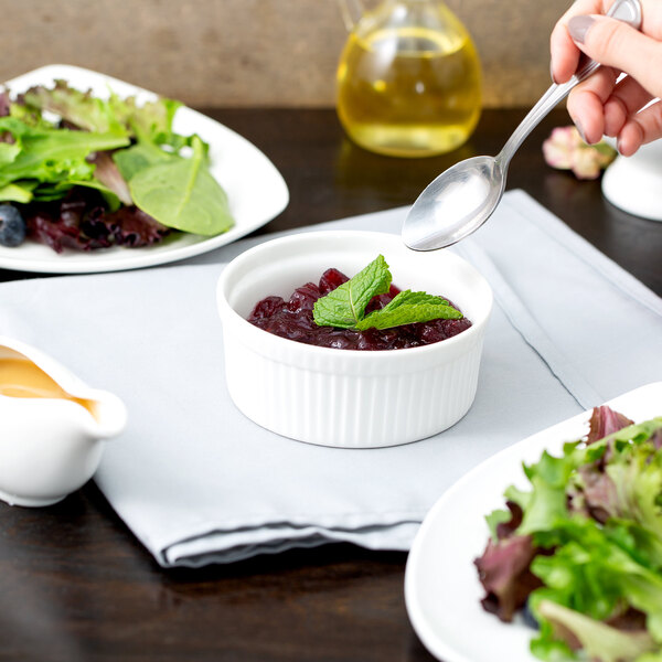 A hand using a spoon to scoop salad into a white fluted ramekin.