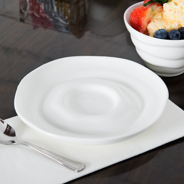 A white porcelain saucer with a spoon and a bowl of fruit.