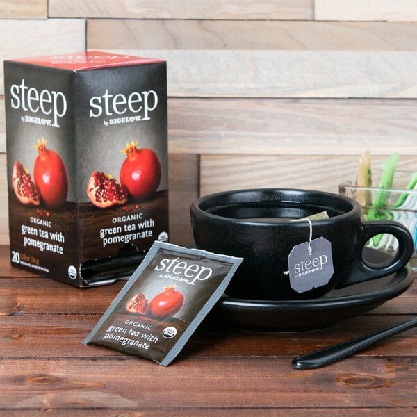 A cup of Steep By Bigelow Organic Green Tea with Pomegranate and a box of tea on a table.