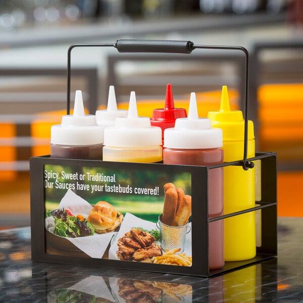 A black metal Tablecraft squeeze bottle caddy on a table with six condiments inside.