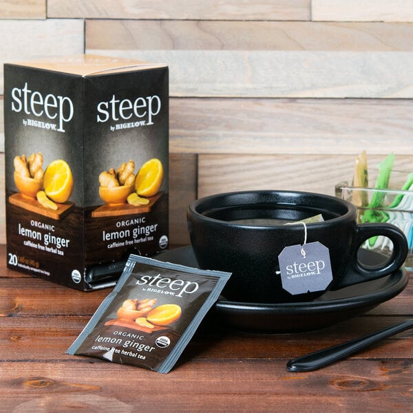 A cup of Steep By Bigelow Organic Lemon Ginger Herbal Tea and a box of tea on a table.