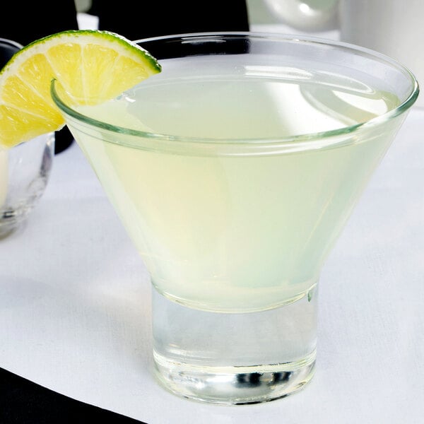 A Libbey martini glass with liquid and a lime wedge on the rim.