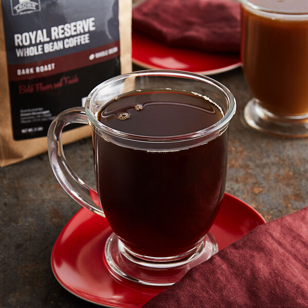 A glass cup of coffee on a red plate next to a bag of Crown Beverages Royal Reserve Guatemalan Whole Bean Coffee.