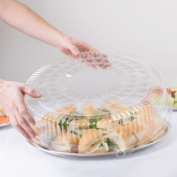 A person holding a Durable Packaging clear plastic high dome lid over a container of food.