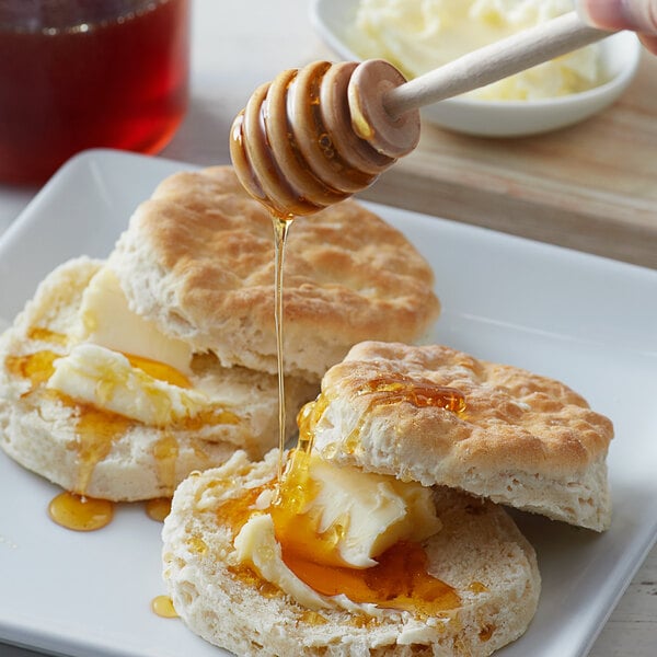 A hand using a wooden spoon to drizzle Monarch's Choice Wildflower Honey over biscuits.
