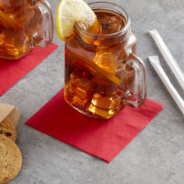 A glass mug with ice and a Choice red 2-ply customizable beverage napkin with a lemon slice on it.