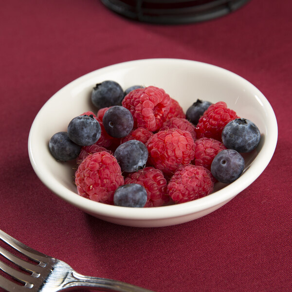 A Tuxton eggshell china bowl filled with raspberries and blueberries on a table with a fork.