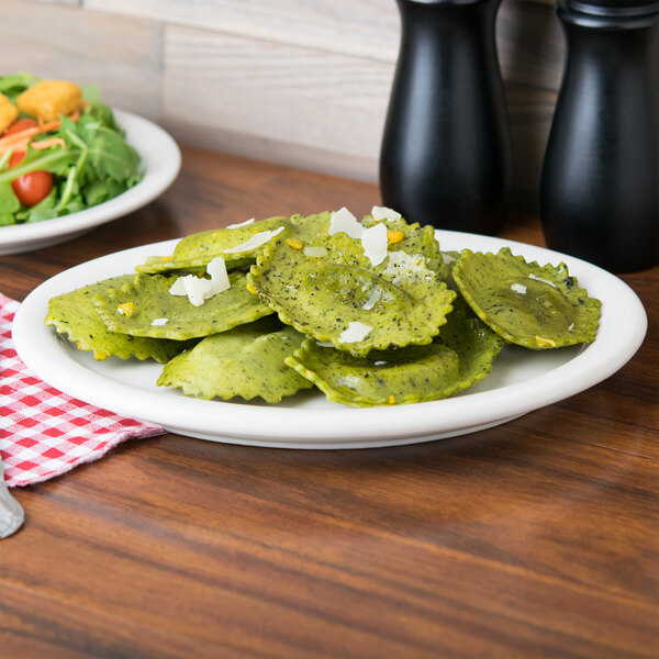 A Tuxton Nevada narrow rim oval china platter with green ravioli, salad, and a glass of wine on a table.