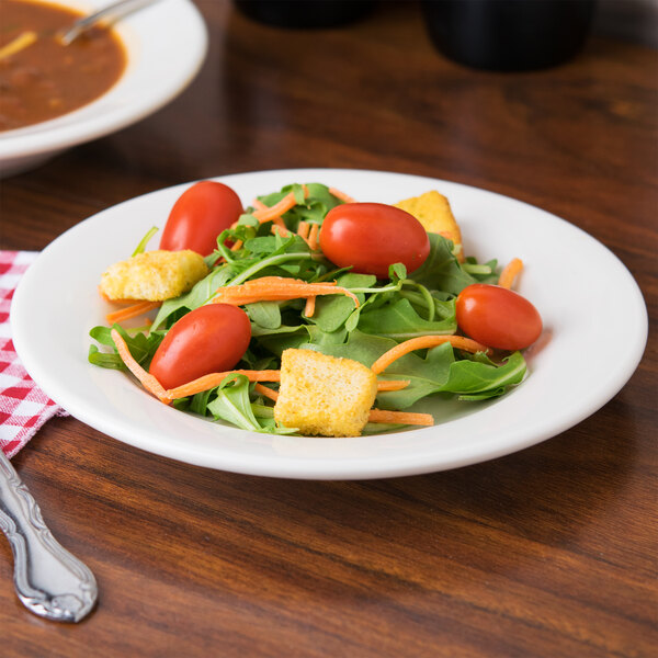 A Tuxton Reno eggshell wide rim china plate with a salad of tomatoes, carrots, and croutons.