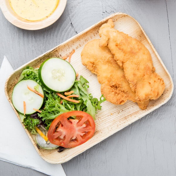 A TreeVive by EcoChoice rectangular palm leaf plate with fried chicken, salad, and dressing on a table.