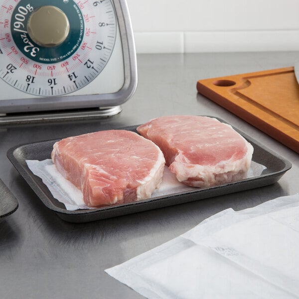 A tray of raw meat on a black foam meat tray next to a scale.