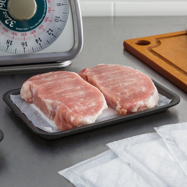 A black foam CKF meat tray with a piece of raw meat on it on a counter.
