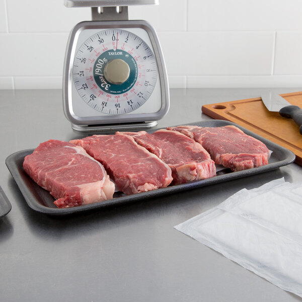 A black foam CKF meat tray with raw meat on a kitchen counter.