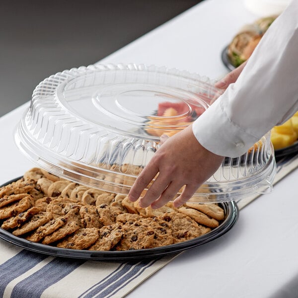 A person holding a Visions clear plastic catering tray filled with cookies.