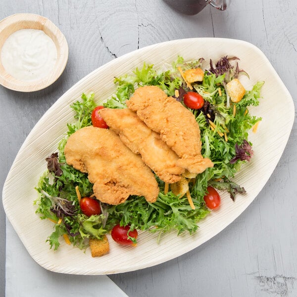 An oval palm leaf tray with fried chicken and salad on it.