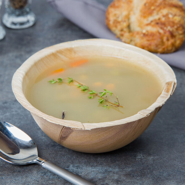 A TreeVive by EcoChoice palm leaf bowl filled with soup with a spoon and a piece of bread.